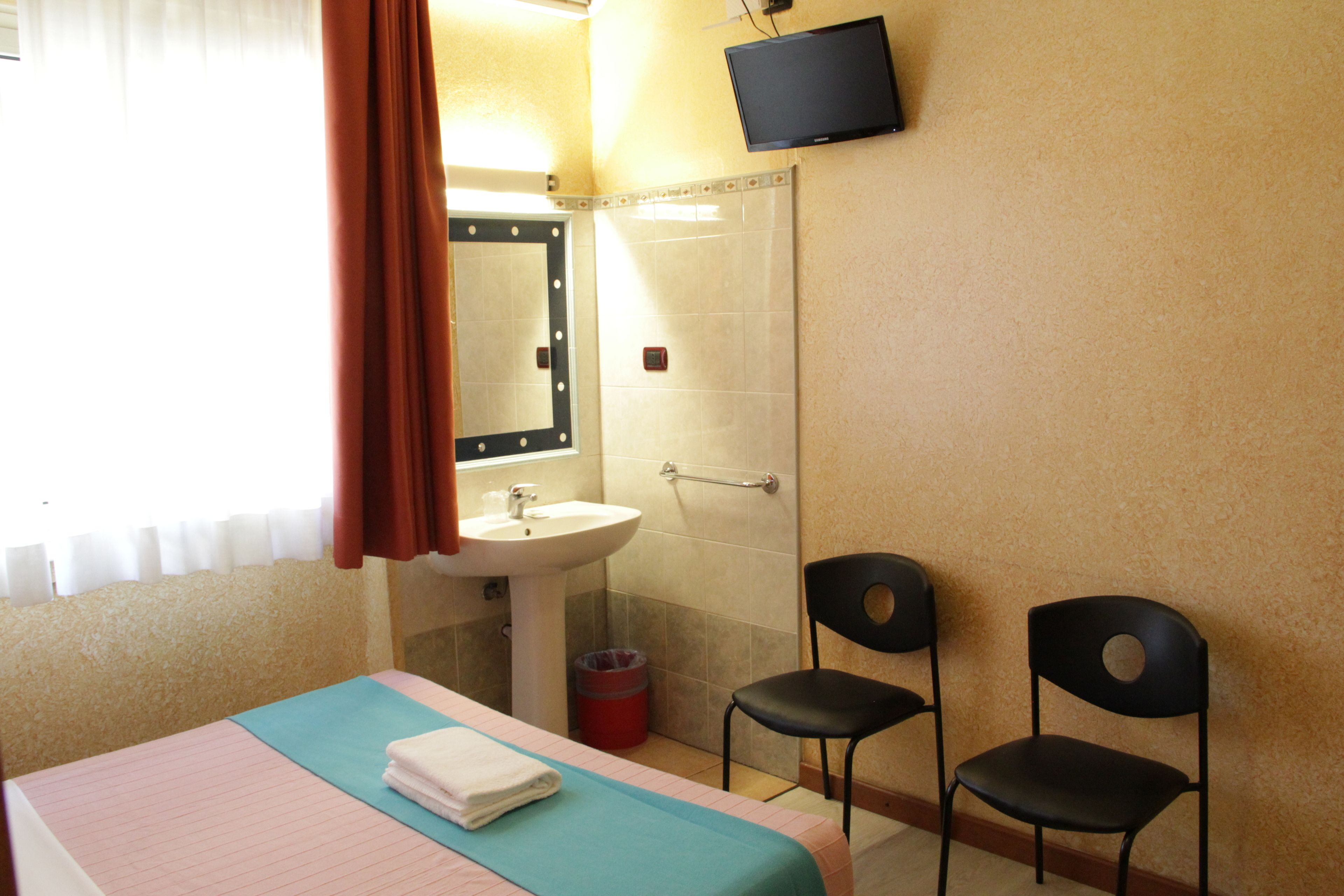 Une chambre d’hôtel avec un lit, un lavabo, deux chaises, une télévision et un miroir.