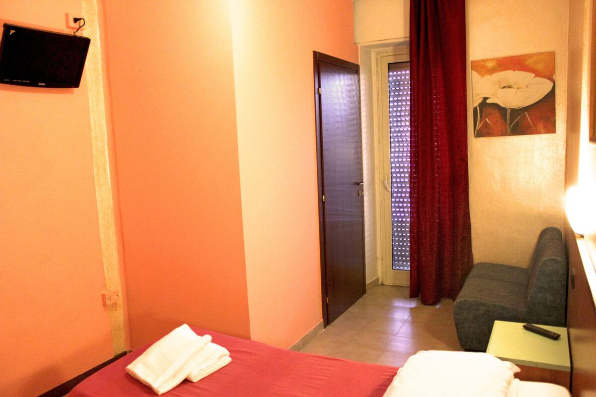 Una camera d'albergo con un letto, una scrivania, una sedia, una televisione e una porta che dà su un bagno.