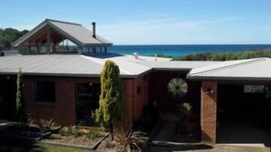 A modern house with a large garage, a circular window, and a view of the ocean. - Sandpiper Ocean Cottages (Douglas River)