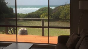 A room with a large window overlooking a grassy area and the ocean. - Sandpiper Ocean Cottages (Douglas River)