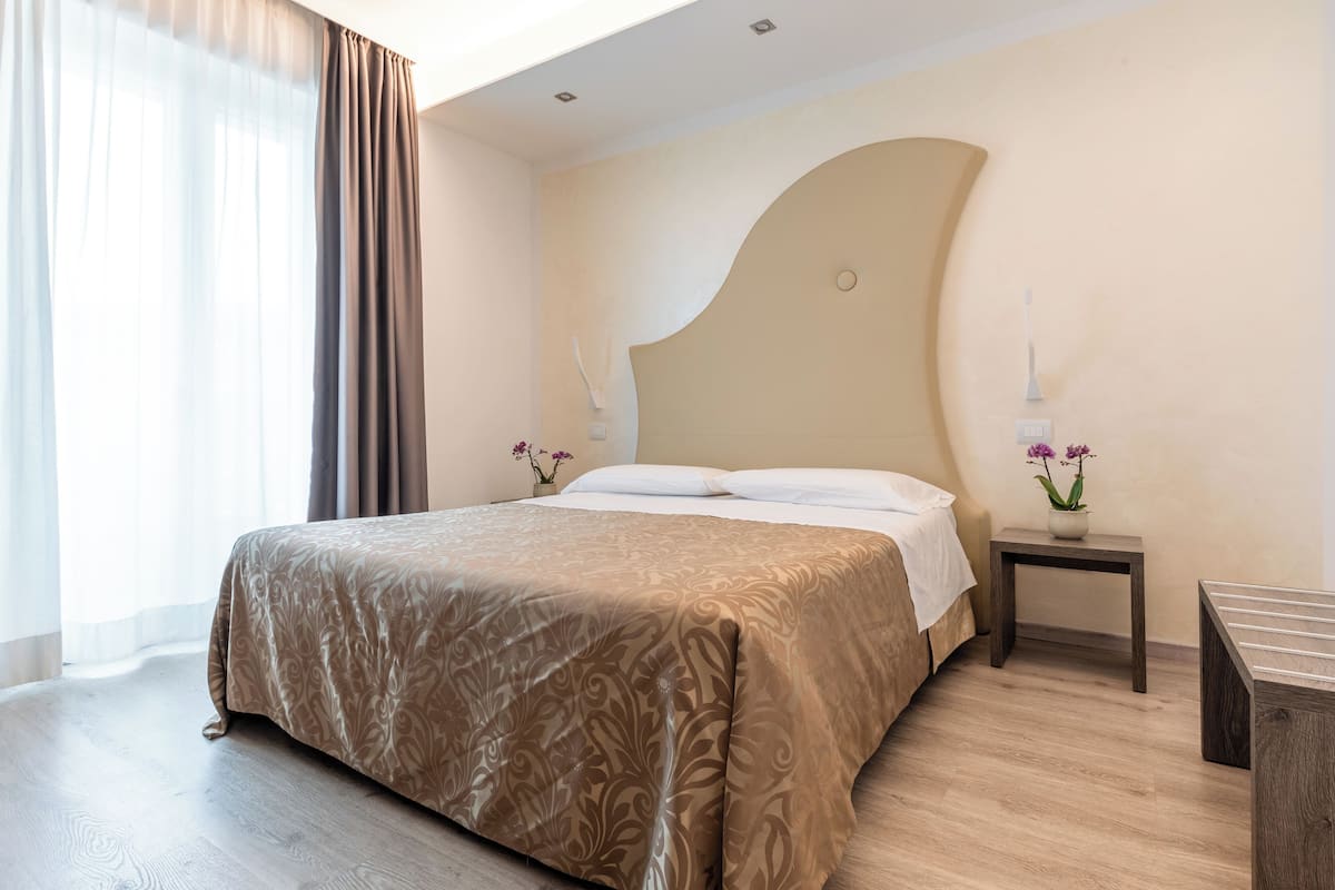 Habitación de hotel con una cama grande, una mesita de noche con lámpara y una pequeña mesa con flores.