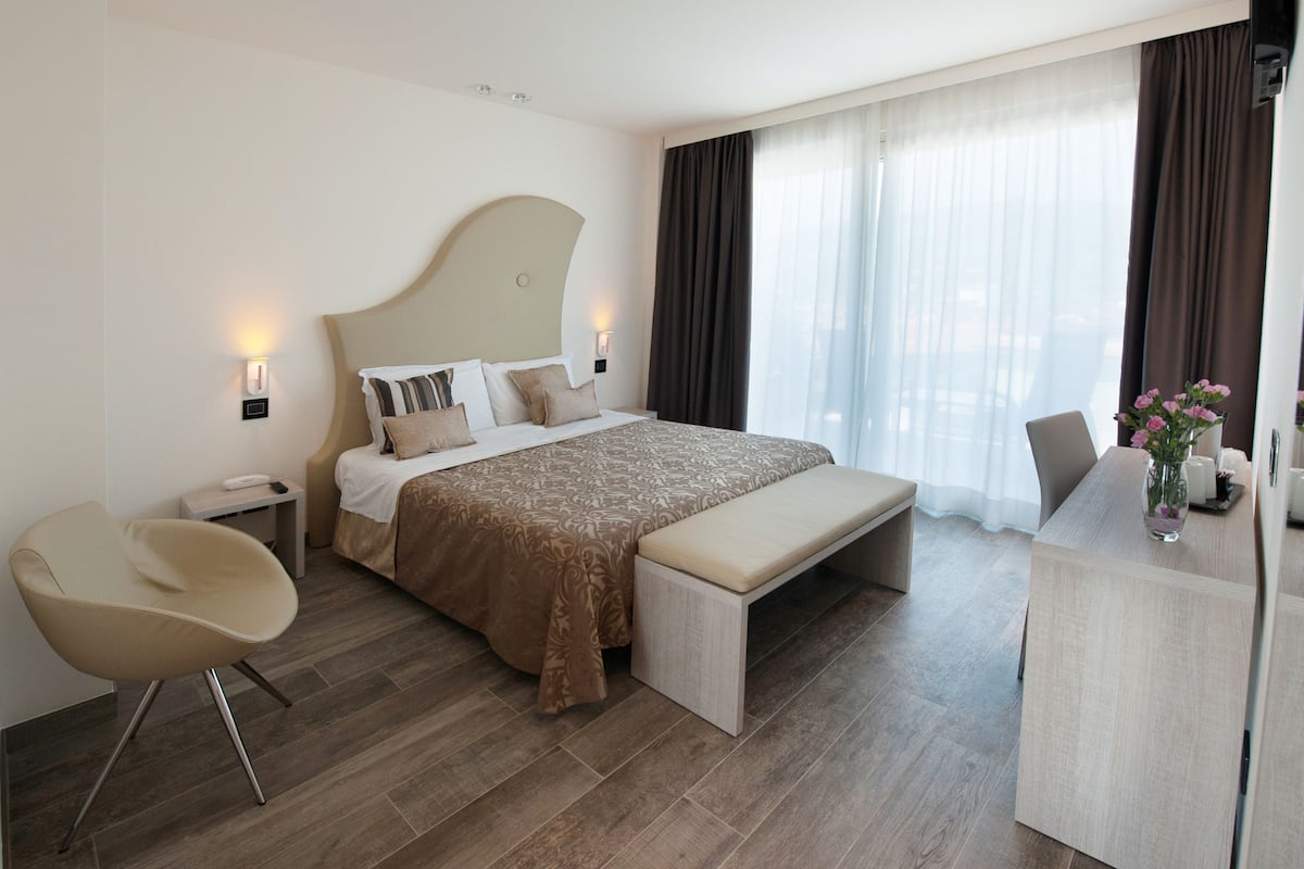 Una habitación de hotel moderna con una cama grande, un banco, una silla, un escritorio y un jarrón de flores.