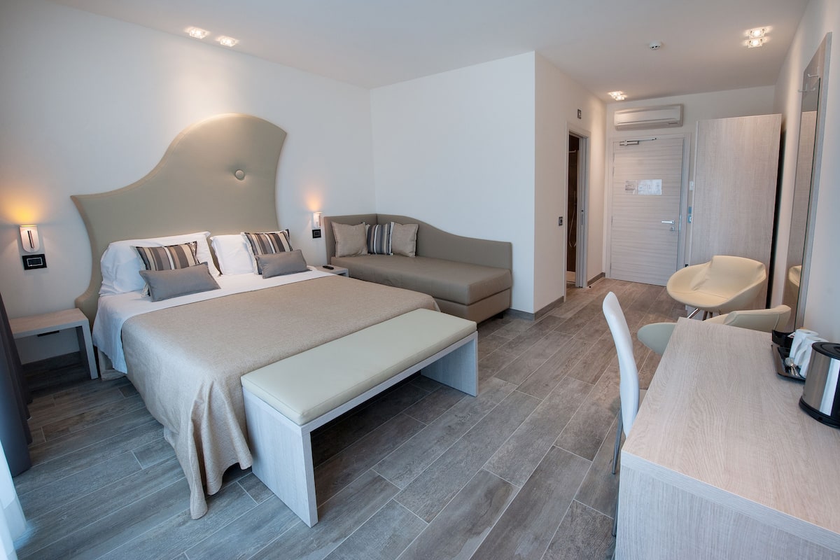 Una habitación de hotel moderna con una cama grande, un sofá, una mesa de comedor y un área de estar separada.