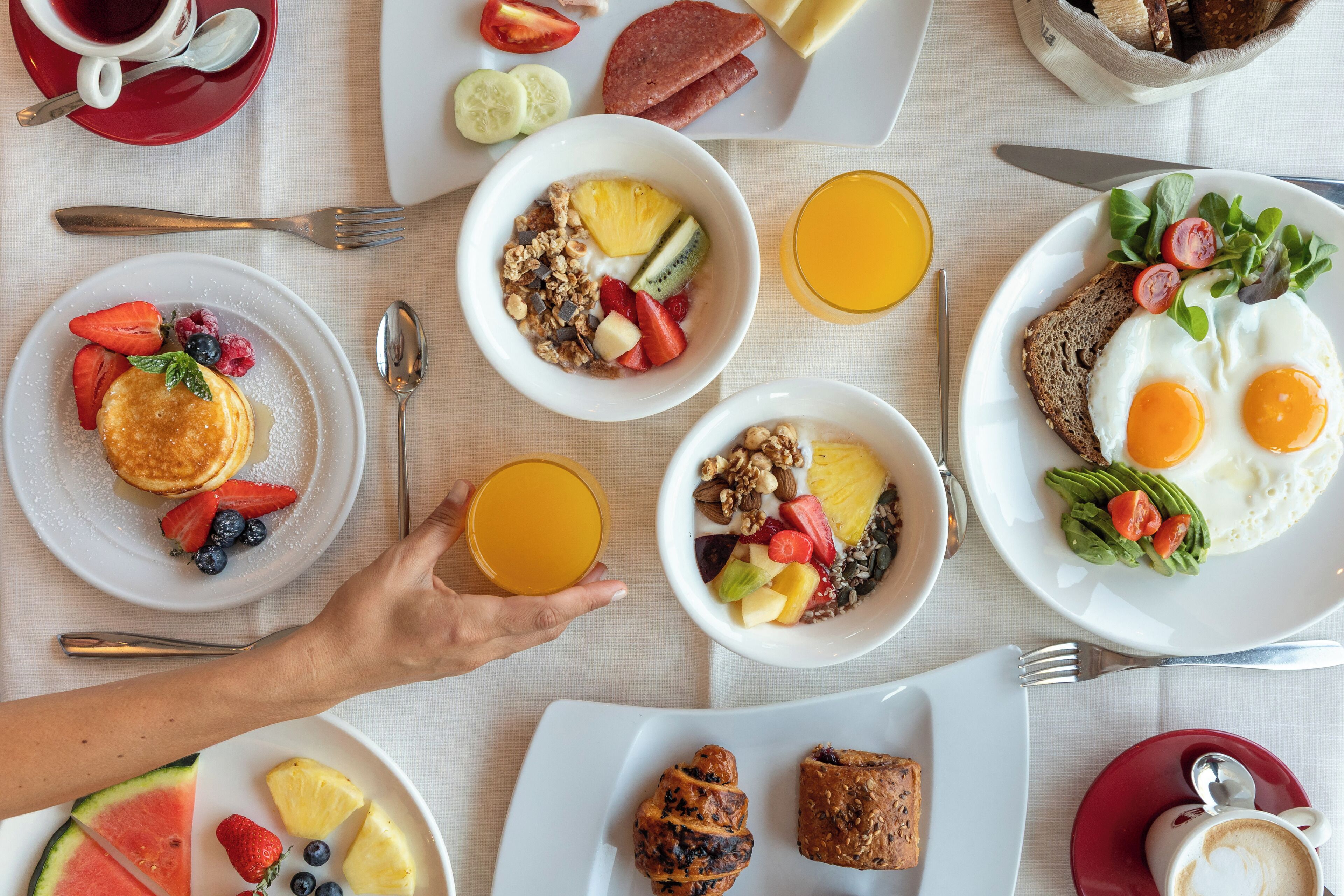Une table dressée pour le petit-déjeuner, avec différents plats, notamment des crêpes, des œufs et des fruits.