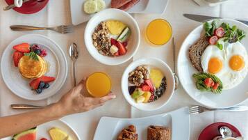 Une table dressée pour le petit-déjeuner, avec différents plats, notamment des crêpes, des œufs et des fruits.