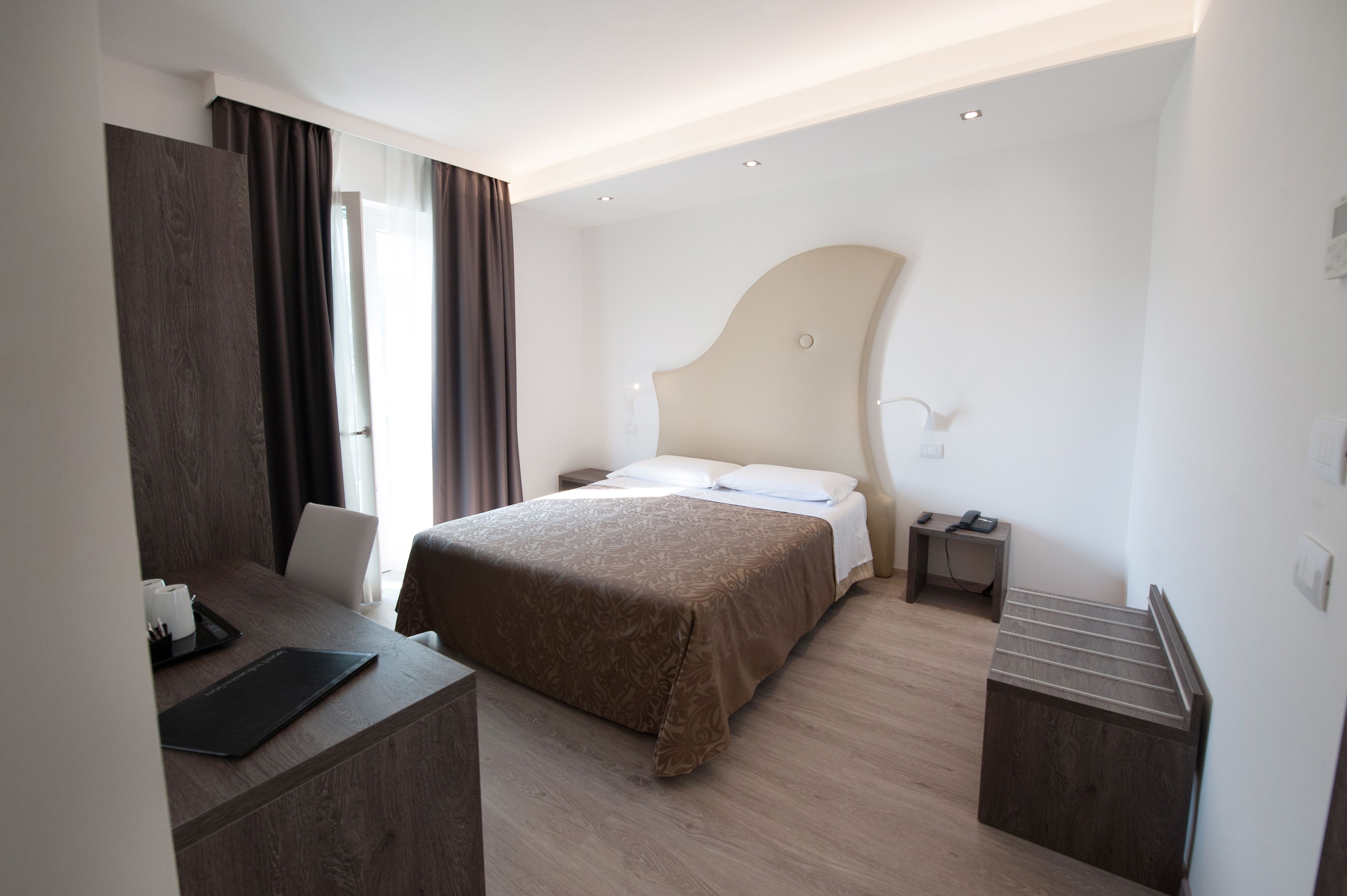 Une chambre d’hôtel moderne avec un grand lit, un bureau avec un ordinateur portable, une table de chevet et une armoire.