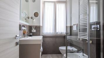 Un baño moderno con un espejo grande, un tocador con lavamanos, un inodoro y una cabina de ducha de vidrio.
