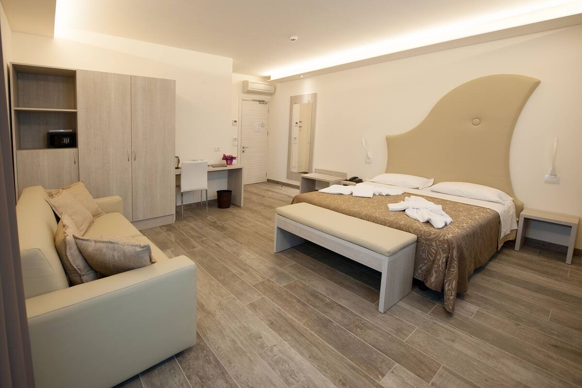 Una habitación de hotel moderna con cama, un banco, un escritorio y un armario.