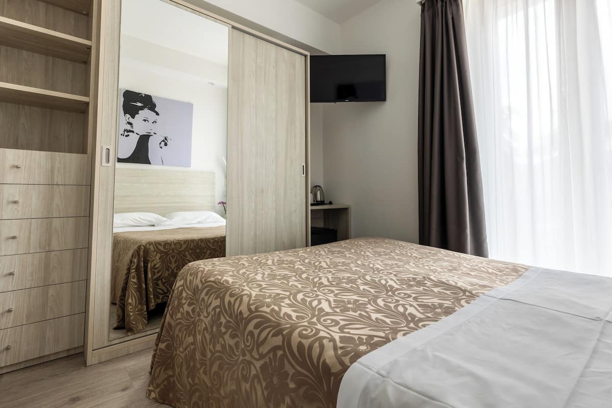 Un dormitorio con cama, armario, televisor y un cuadro en la pared.