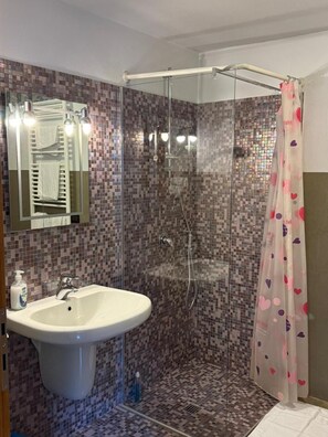 Un baño con ducha de mampara de vidrio, un lavamanos blanco y una pared de mosaico con azulejos.