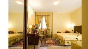 A hotel room with two beds, a desk, a chair, a TV, and a window with curtains. - La Madonnina (Budduso)