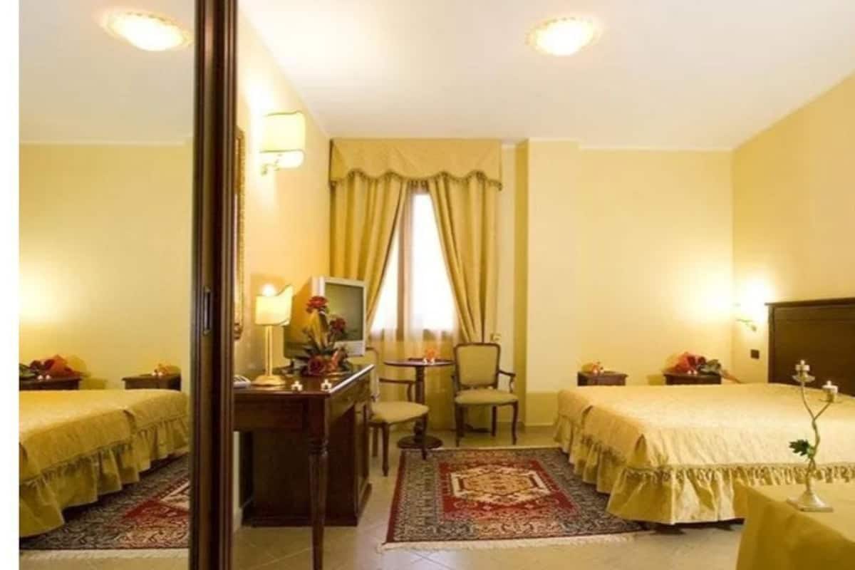 Une chambre d’hôtel avec deux lits, un bureau, une chaise, une télévision et une fenêtre avec des rideaux.