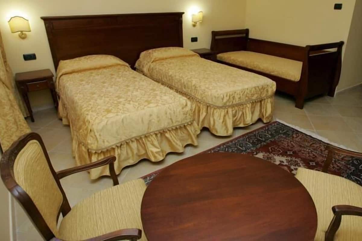 Une chambre avec deux lits simples, un petit canapé, une table ronde en bois et deux chaises.
