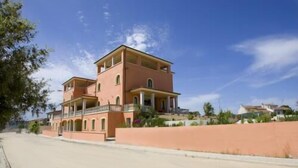 A two-story building with a balcony and a flat roof, surrounded by a low wall and greenery. - La Madonnina (Budduso)