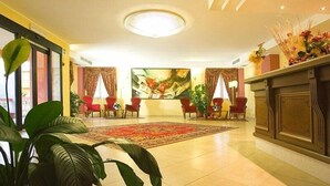 A hotel lobby with a large abstract painting, red chairs, a fireplace, and a large potted plant. - La Madonnina (Budduso)