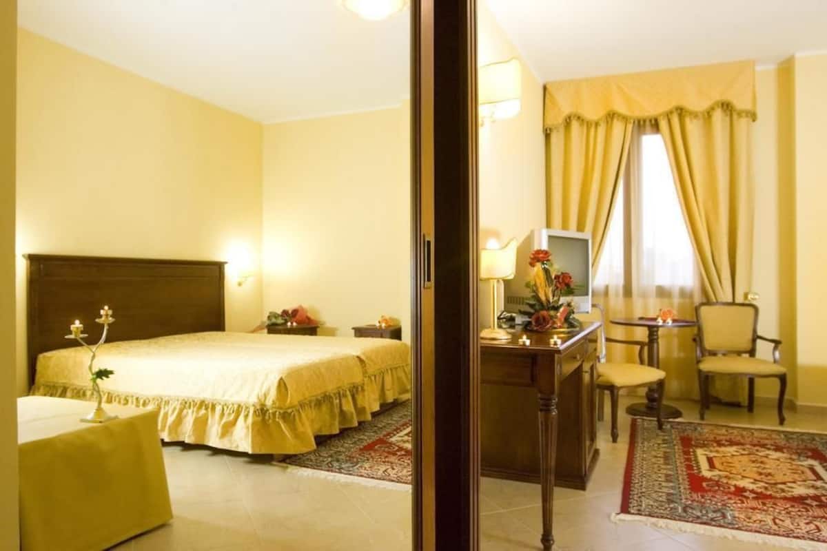 Une chambre d’hôtel comprenant un lit, une table de chevet, une lampe, un bureau, une chaise et une vue sur l’extérieur par une fenêtre munie de rideaux.