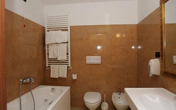 Un baño con bañera, inodoro, bidé y un perchero con toallas.