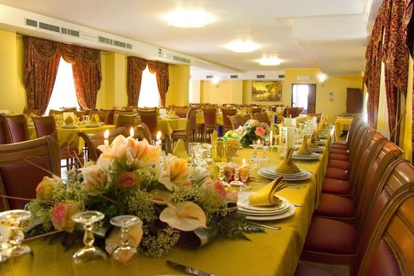A formal dining room with multiple tables set for service, featuring floral centerpieces and formal table settings. - La Madonnina (Budduso)