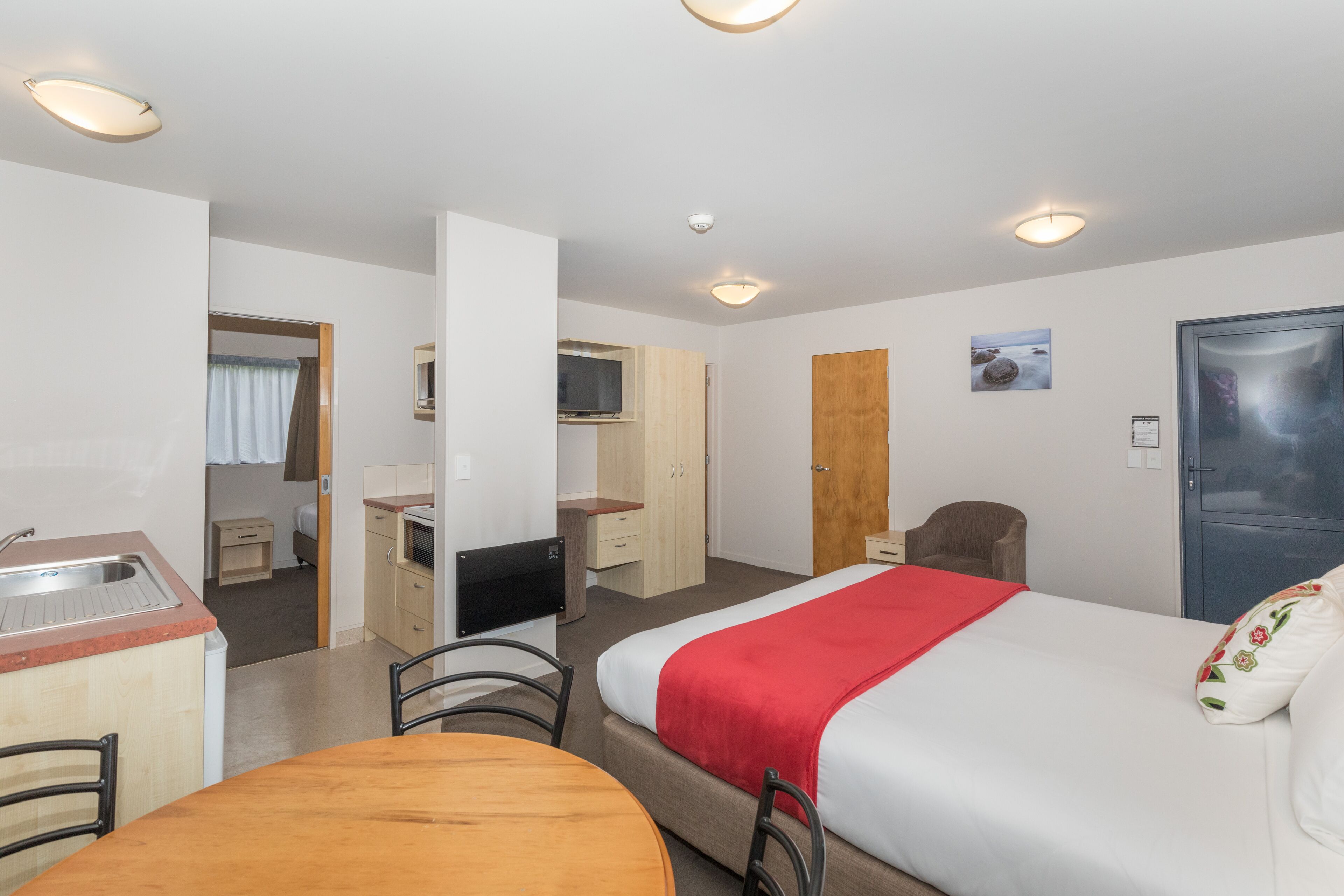 Een hotelkamer met een bed, een bureau, een stoel, een kleine kitchenette en een deur.