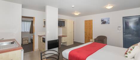 Een hotelkamer met een bed, een bureau, een stoel, een kleine kitchenette en een deur.