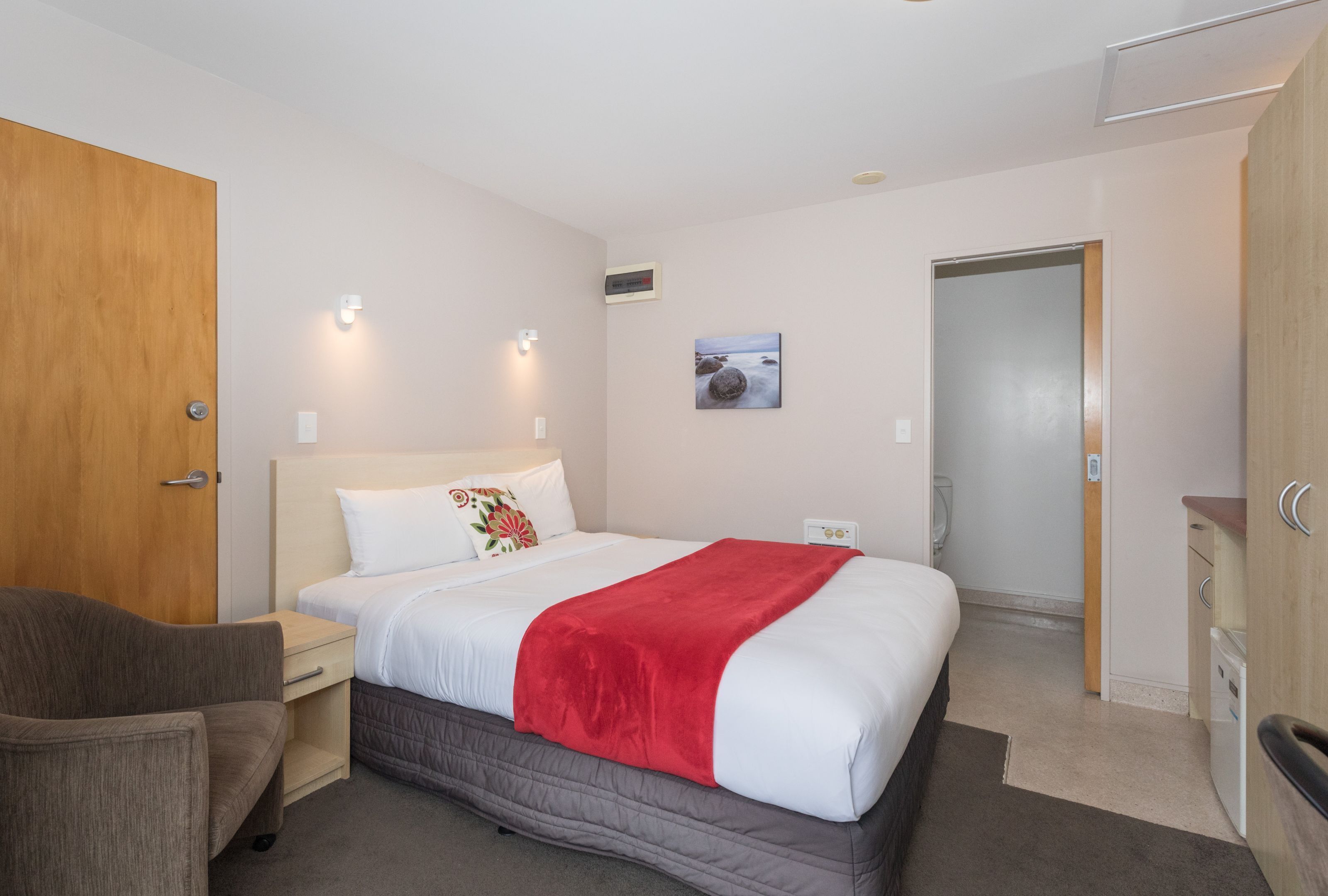 A hotel room with a bed, a chair, a desk, and a wardrobe.