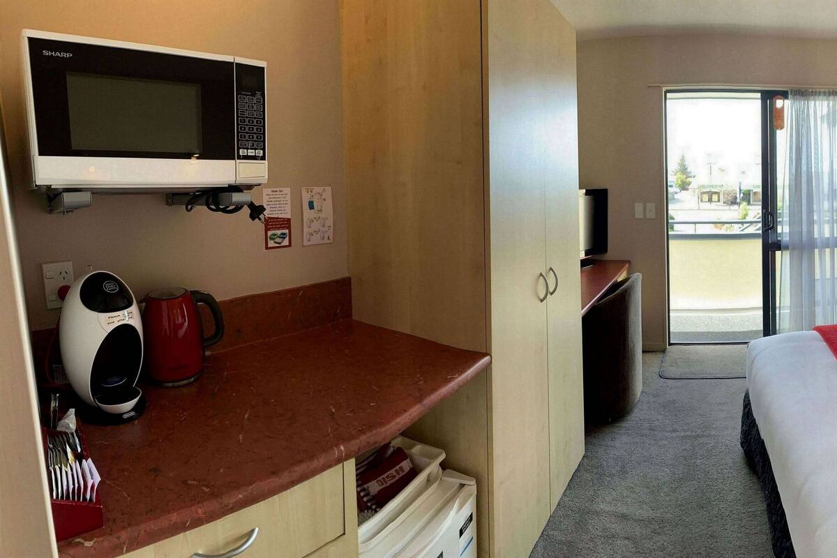 A hotel room with a bed, a desk with a microwave, a coffee maker, and a view of the outside.