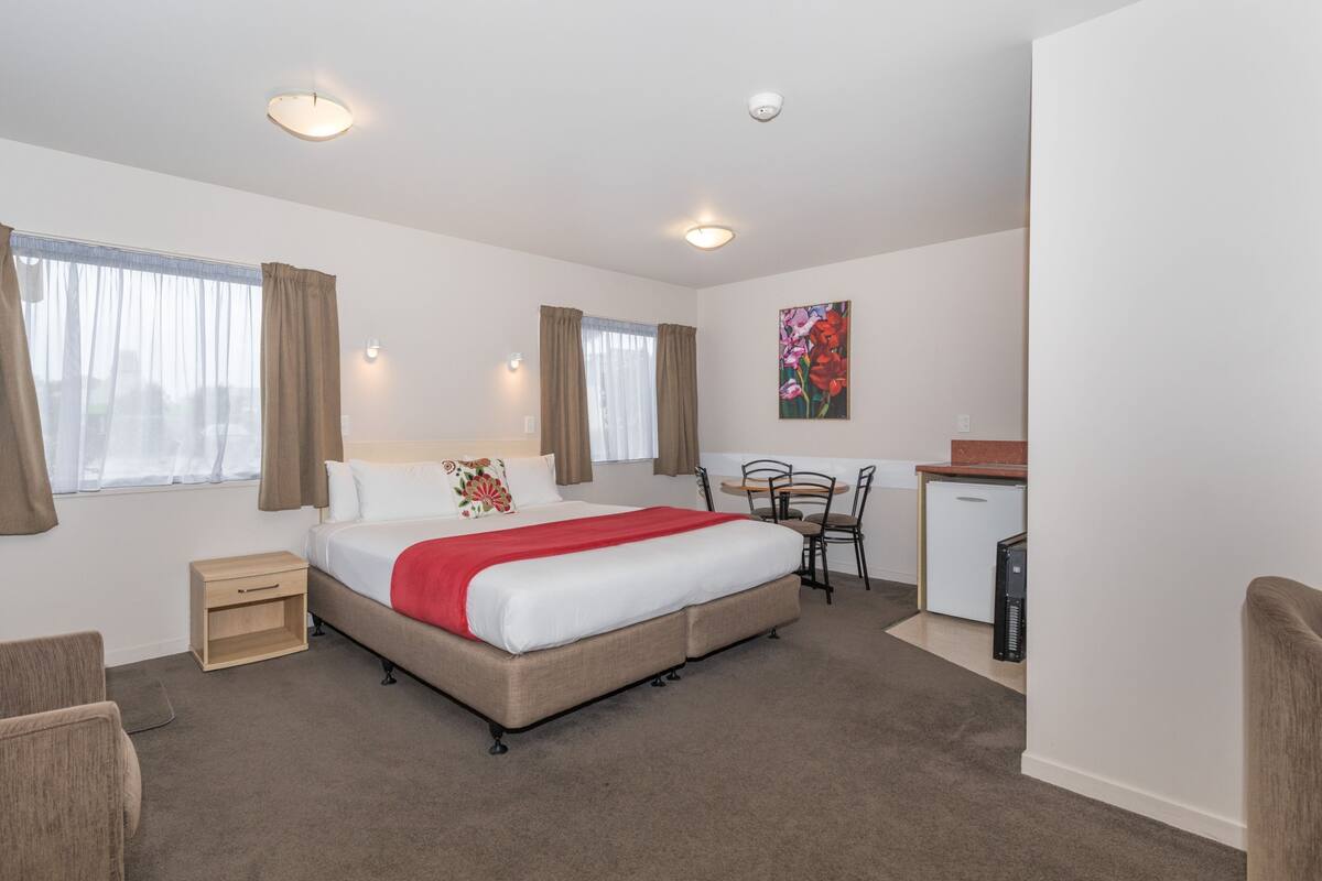 A hotel room with a bed, bedside table, chair, desk, and a small kitchenette.