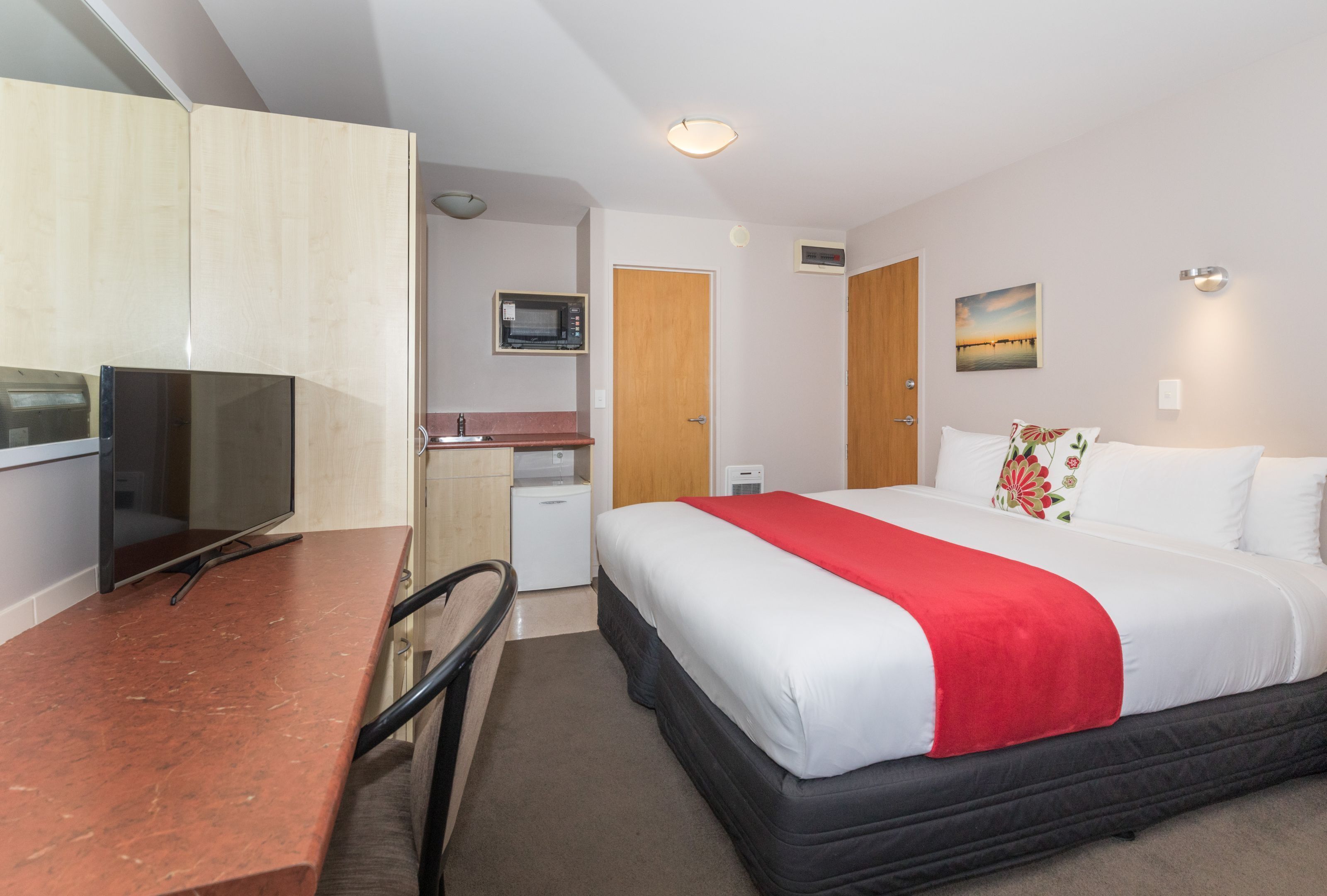 A hotel room with a bed, a desk with a television, a microwave, and a small kitchenette.
