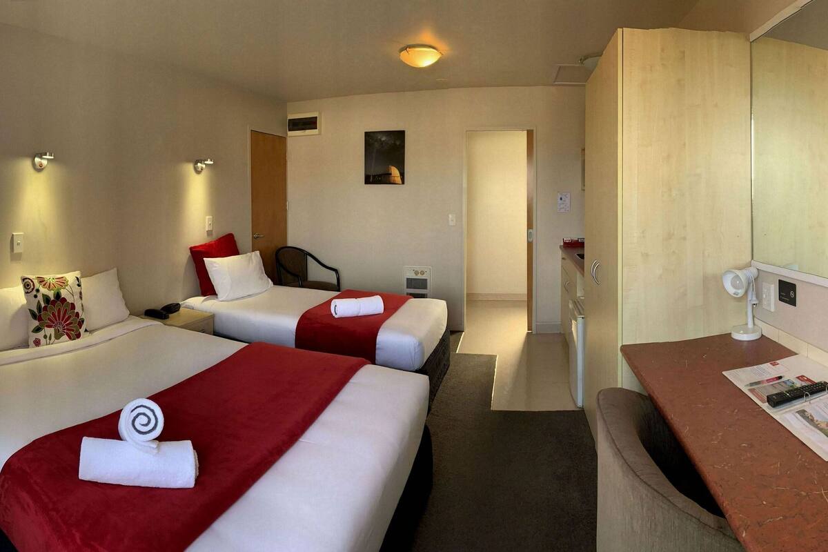 A hotel room with two beds, a desk, a chair, a TV, and a mirror.