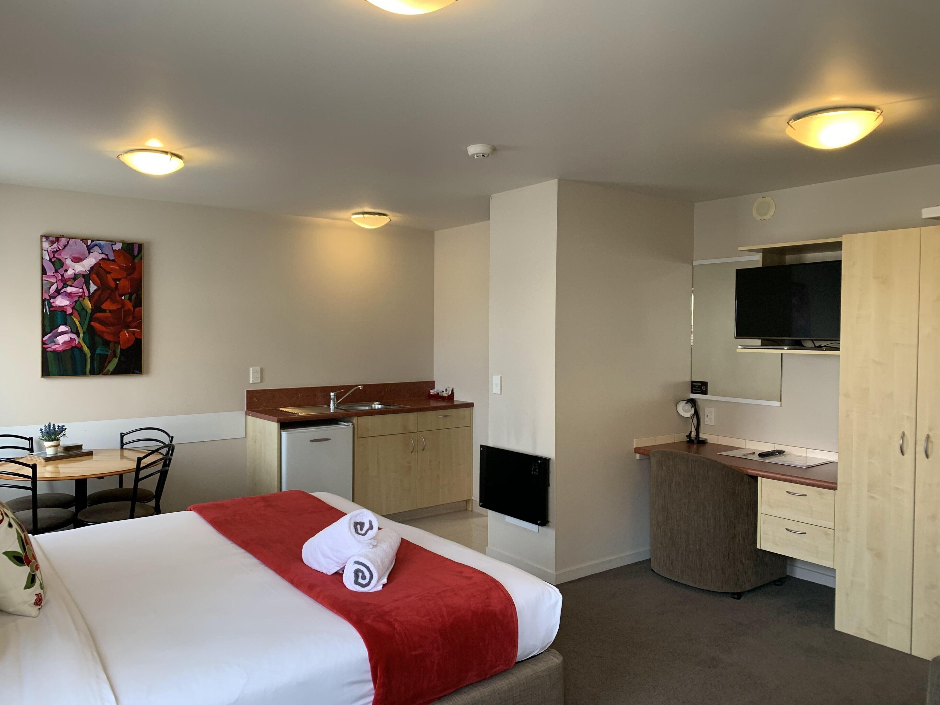 A hotel room with a bed, a small kitchenette, a dining area, and a TV.