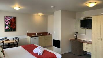 A hotel room with a bed, a small kitchenette, a dining area, and a TV.