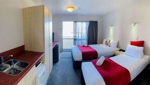 A hotel room with two beds, a sink, a chair, and a view of the outdoors. - Bella Vista Motel Oamaru (Oamaru)