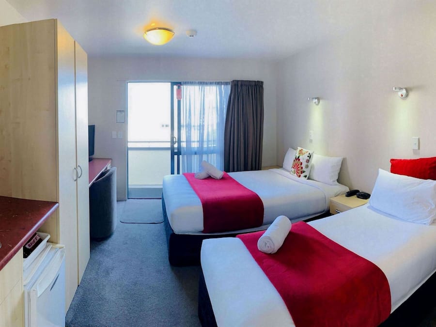 Hotellihuone, jossa on kaksi sänkyä, pesuallas, tuoli ja näkymä ulos.