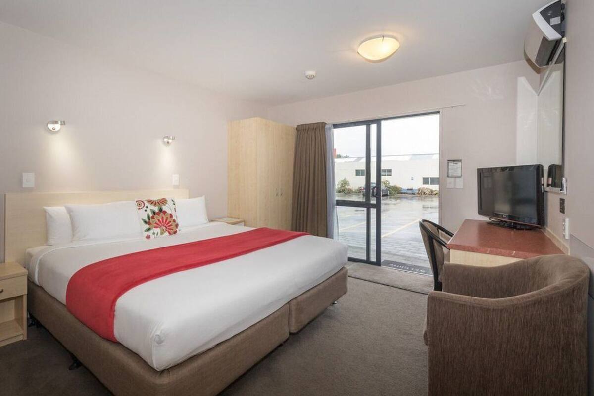 A hotel room with a bed, a desk with a television, and a sliding glass door to the outside.
