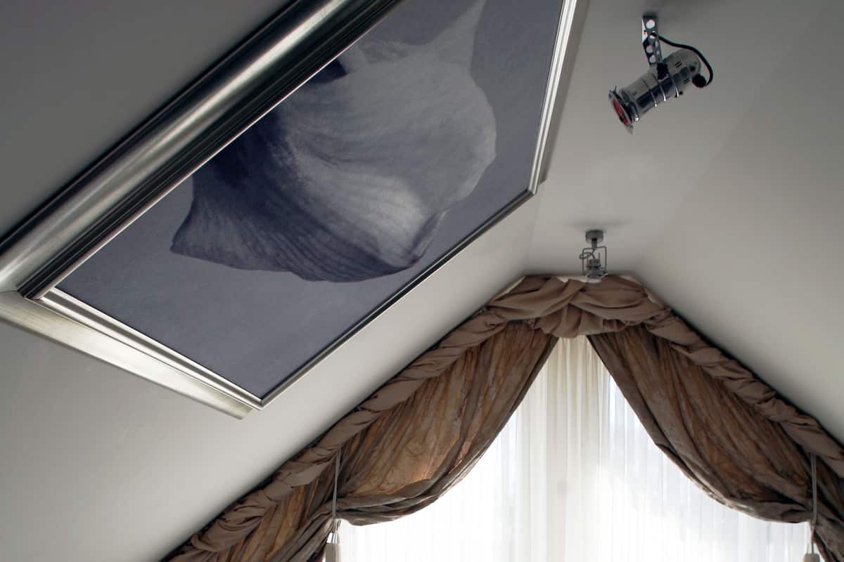 Une chambre avec un plafond en pente, un lit, une chaise et une fenêtre avec des rideaux.