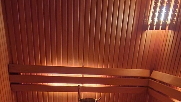 Eine Sauna mit Holzbänken und einer Sitzbank, einem kleinen Metallbehälter und einer Schale mit Steinen.