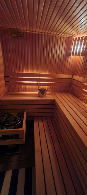 Eine Sauna mit Holzbänken, einer Sitzbank, einem kleinen Metallbehälter und einer Schale mit Steinen.