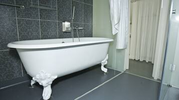 A white freestanding bathtub in a bathroom with dark patterned tiles and a glass shower door.