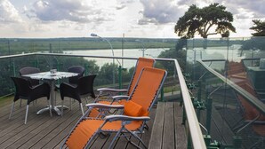 Eine Terrasse mit Tisch und Stühlen mit Blick auf einen Fluss und Grünflächen.