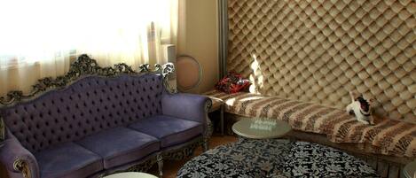 Uma sala de estar com um sofá roxo, um banquinho estampado e uma mesa de centro redonda.