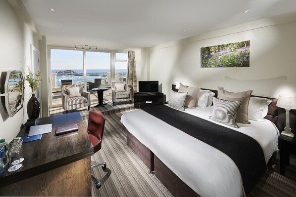 Une chambre d’hôtel avec un grand lit, un bureau avec un ordinateur portable, une télévision et une vue sur la mer.