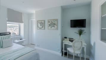 Un dormitorio con cama, escritorio, silla, televisor y obras de arte en la pared.
