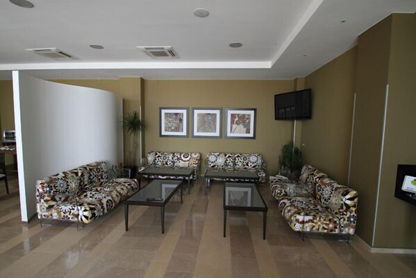 A modern living room with patterned sofas and glass-top coffee tables, a flat-screen TV mounted on the wall, and framed artwork above the seating area. - Tenuta Inagro (San Severo)