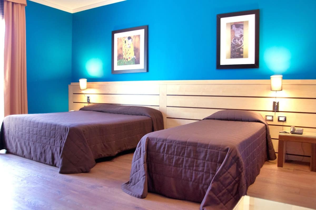 A hotel room with two beds, a wooden headboard, and two framed pictures on the wall.