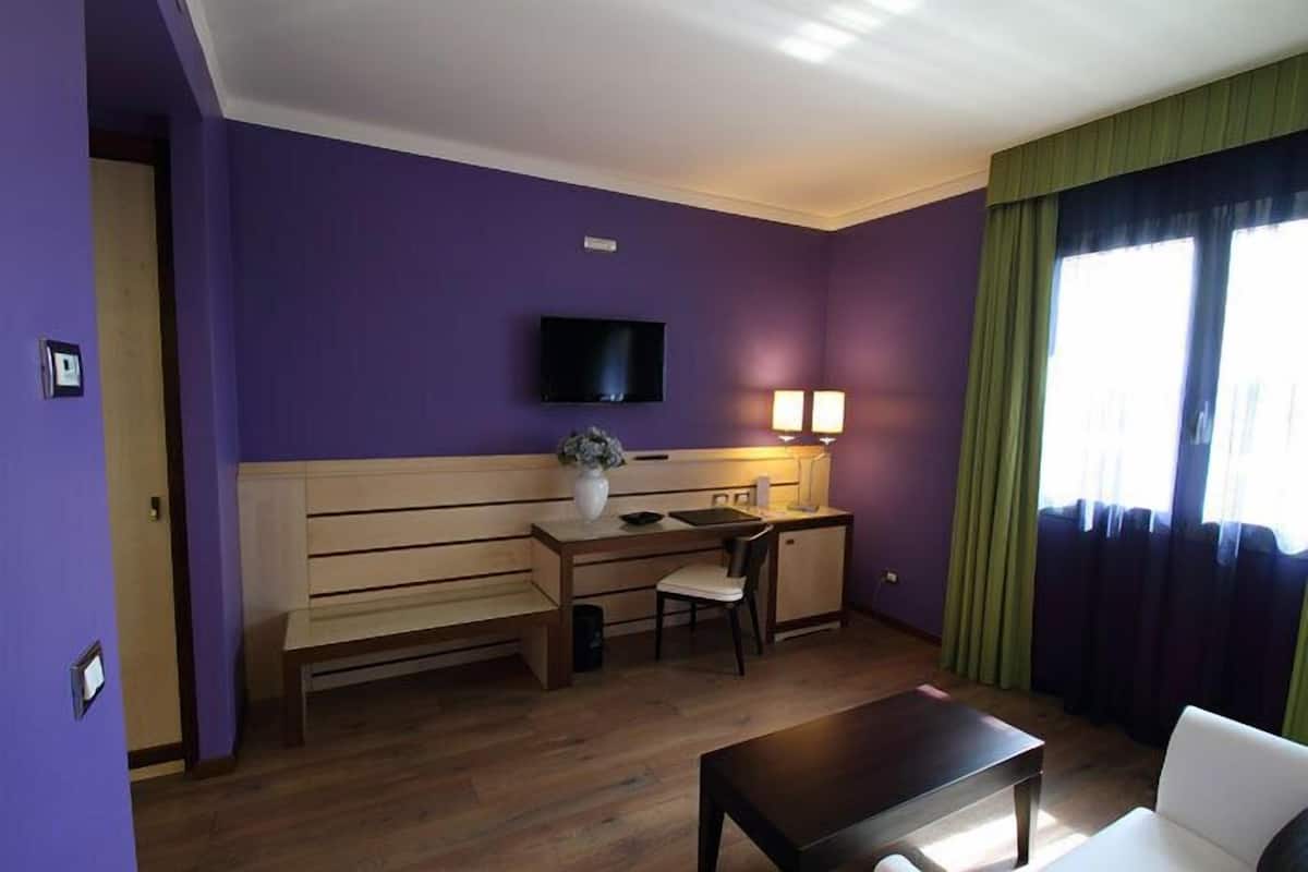 A room with a wooden bench, a desk with a chair, a television mounted on the wall, and a window with curtains.