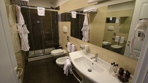 A modern bathroom with a glass-enclosed shower, a toilet, a sink with toiletries, and a large mirror.