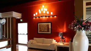 A room with a red wall, a white sofa, a chandelier, a framed picture, and a vase with flowers. - Tenuta Inagro (San Severo)