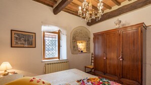 A bedroom with a bed, a wooden wardrobe, a chandelier, a window with curtains, and a framed picture on the wall.