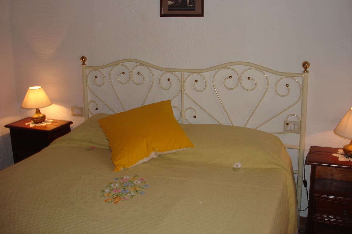 Ein Bett mit einem gelben Kopfkissen, einem floral bestickten Kissenbezug und einem Nachttisch mit einer Lampe.