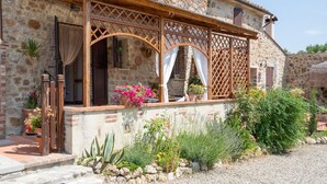 A stone building with a wooden porch, potted plants, and a gravel pathway.